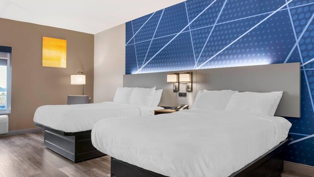 Une chambre d’hôtel avec deux lits, une grande fenêtre, un mur orné d’un motif géométrique et une lampe.