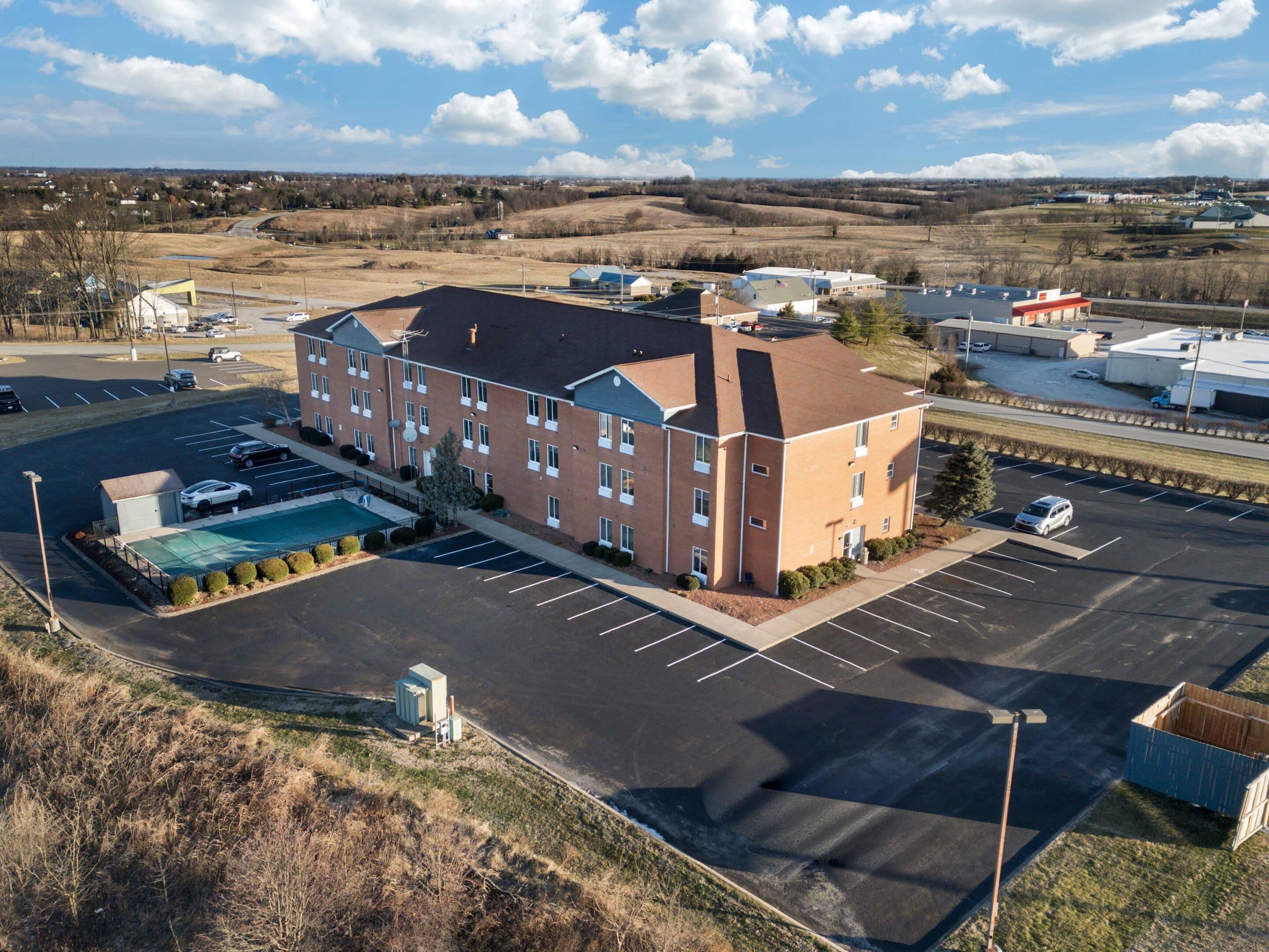 A multi-story hotel with a swimming pool, parking lot, and a view of the surrounding landscape.