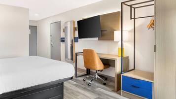 A hotel room with a bed, a desk, a chair, a TV, a wardrobe, and a lamp.