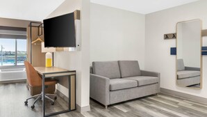 Une chambre d’hôtel moderne équipée d’un bureau, d’une chaise, d’un canapé, d’un téléviseur à écran plat et d’un grand miroir.