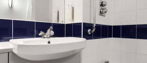 Un baño con lavamanos blanco, un espejo, ducha de mano y bañera.