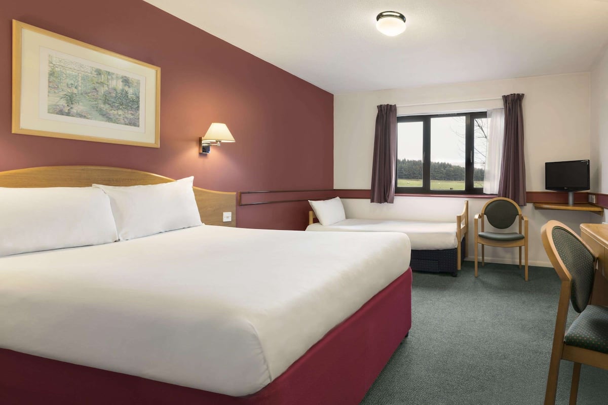 Ein Hotelzimmer mit zwei Betten, einem Schreibtisch, einem Stuhl, einem Fernseher und einem Fenster mit Vorhängen.