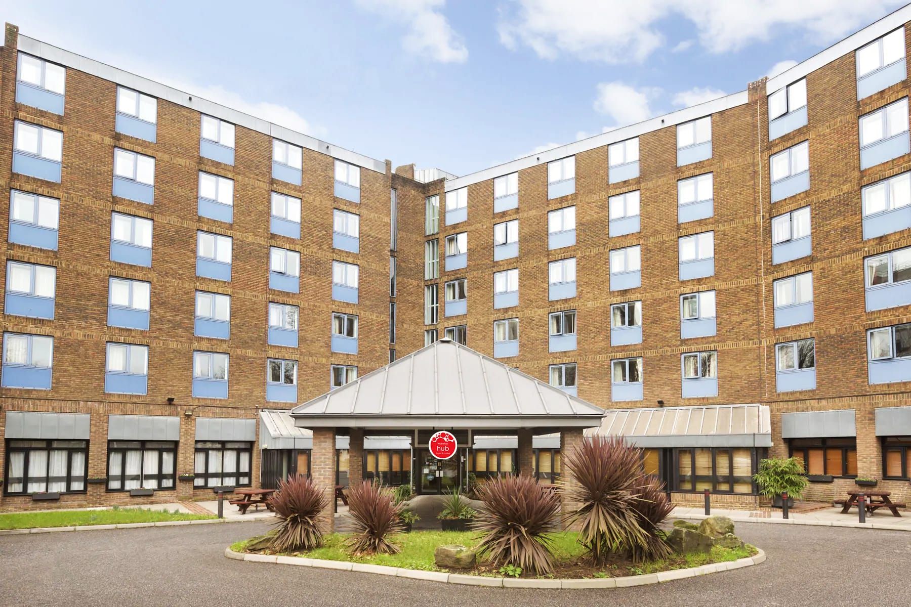 A multi-story building with a central courtyard, featuring a hub sign, outdoor seating, and a well-maintained garden.