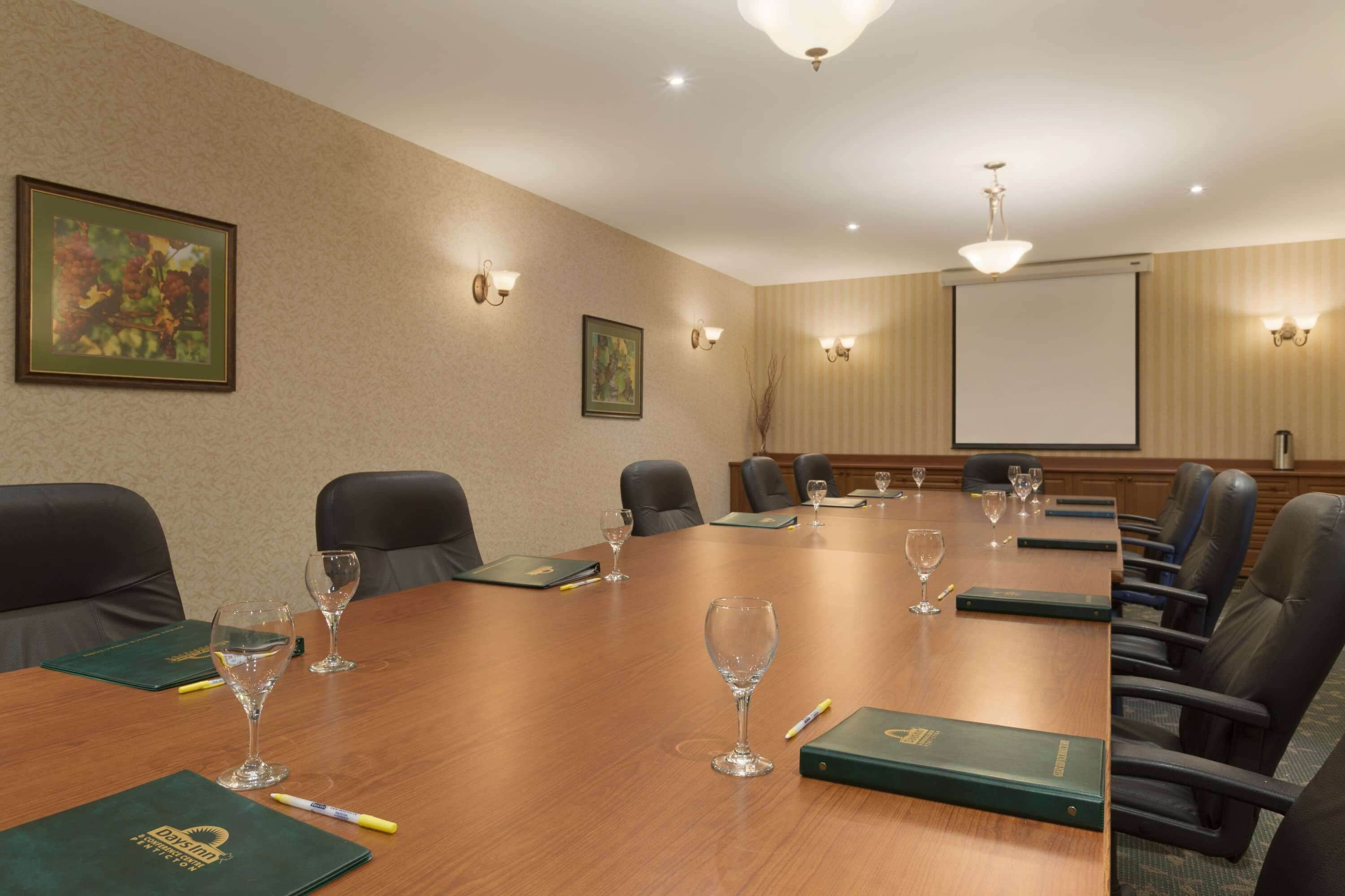 Una sala conferenze con un lungo tavolo, poltrone in pelle nera e uno schermo proiettore a parete.