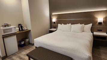 A hotel room with a large bed, bedside tables, a microwave, a small refrigerator, and a bench.