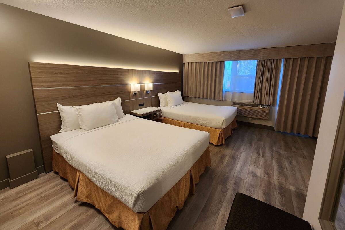 Una habitación de hotel con dos camas, un ventanal con cortinas, cabecero de madera y un aire acondicionado instalado en la pared.