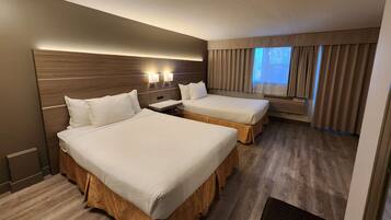 Una habitación de hotel con dos camas, un ventanal con cortinas, cabecero de madera y un aire acondicionado instalado en la pared.