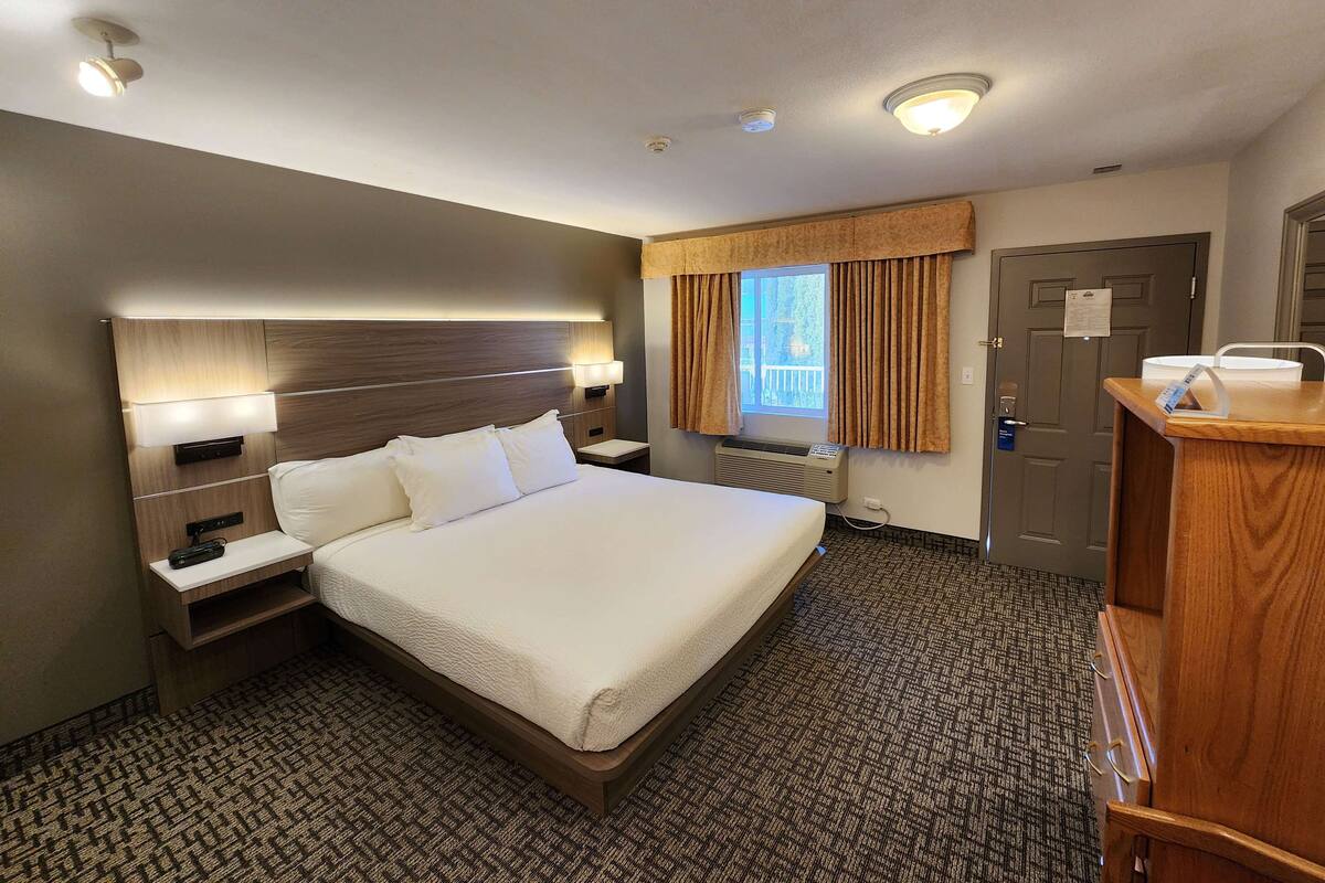Habitación de hotel con una cama grande, mesitas de noche, un escritorio, una ventana con cortinas y una puerta.