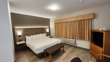 A hotel room with a bed, bedside tables, a bench, a TV cabinet, and a window with curtains.