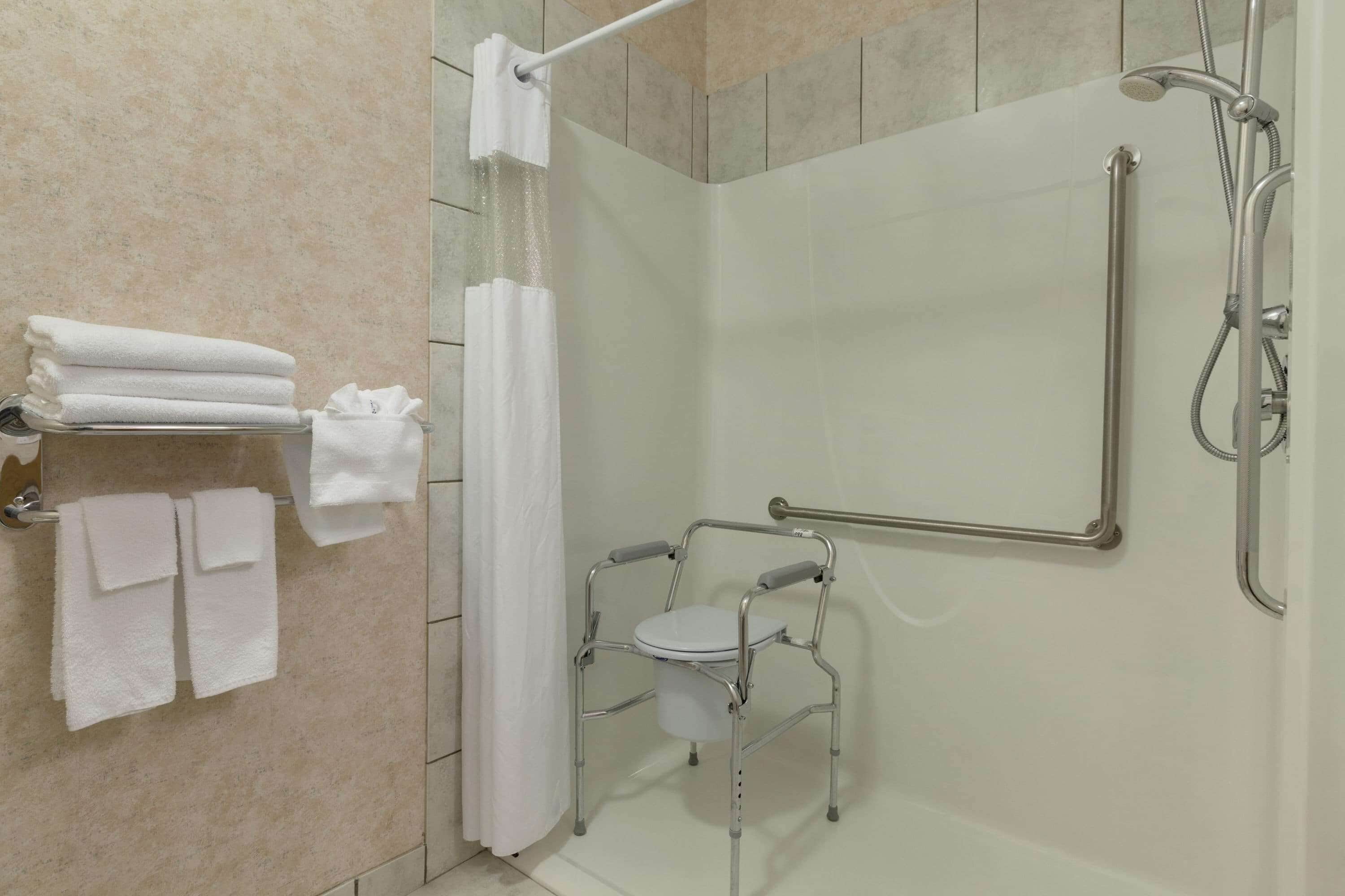 A bathroom with a shower, a grab bar, and a wheelchair-accessible toilet.