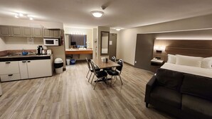 Une chambre d’hôtel comprenant un lit, une table à manger avec des chaises, un coin cuisine, une salle de bain et un grand miroir.