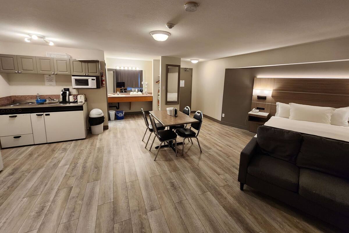 Una habitación de hotel con cama, una mesa de comedor con sillas, kitchenette, baño y un espejo grande.