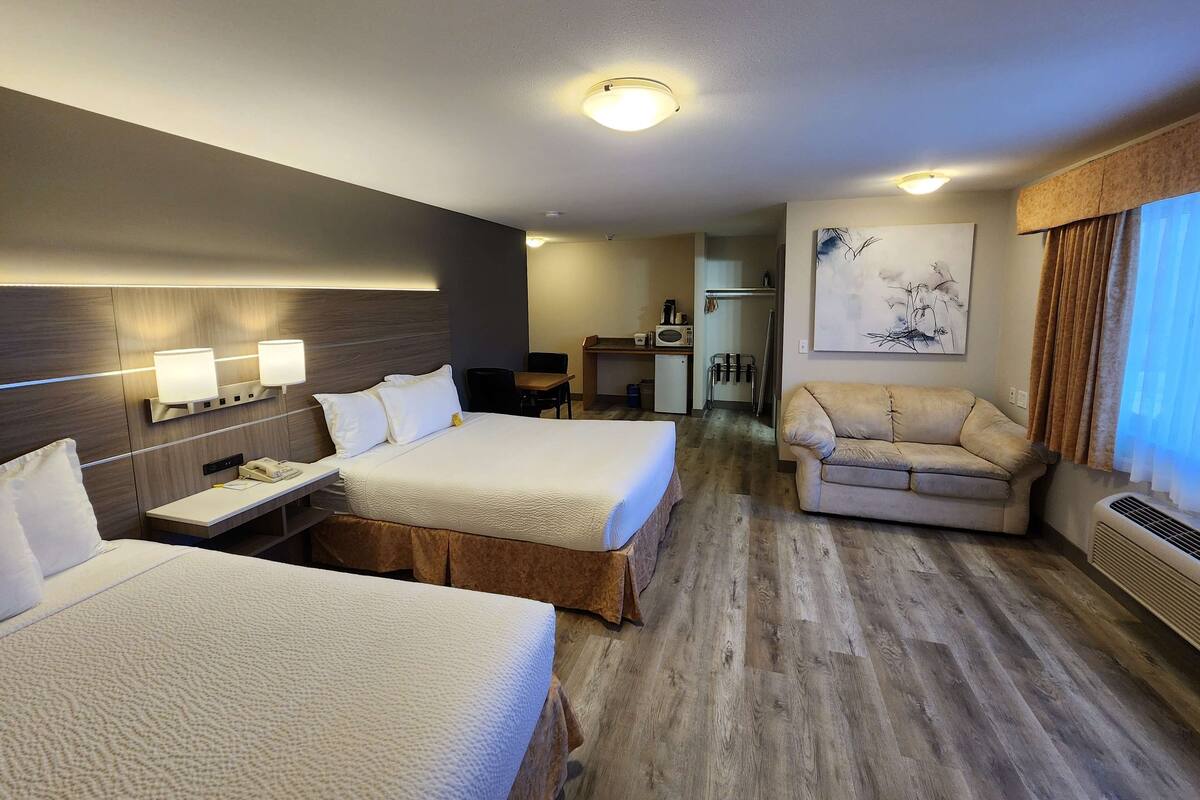 Habitación de hotel con dos camas, un sofá, un escritorio, un microondas y un cuadro en la pared.