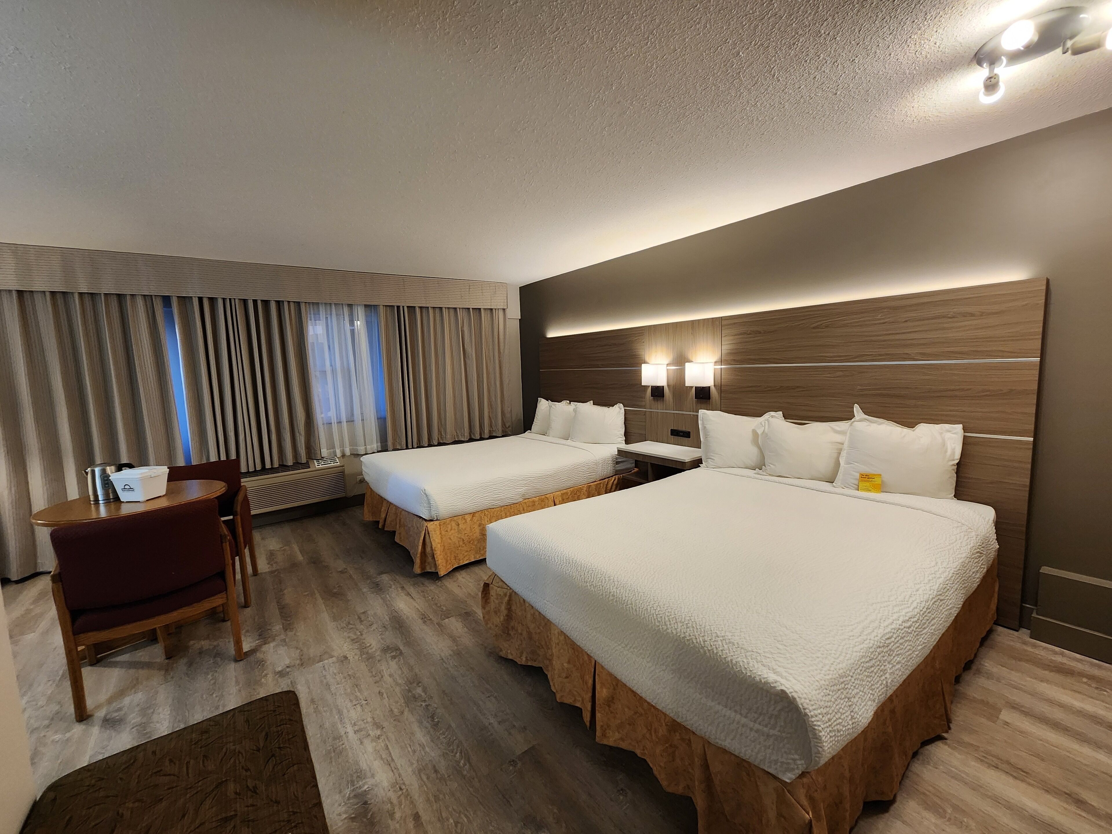 Habitación de hotel con dos camas, un escritorio, una silla y un ventanal con cortinas.