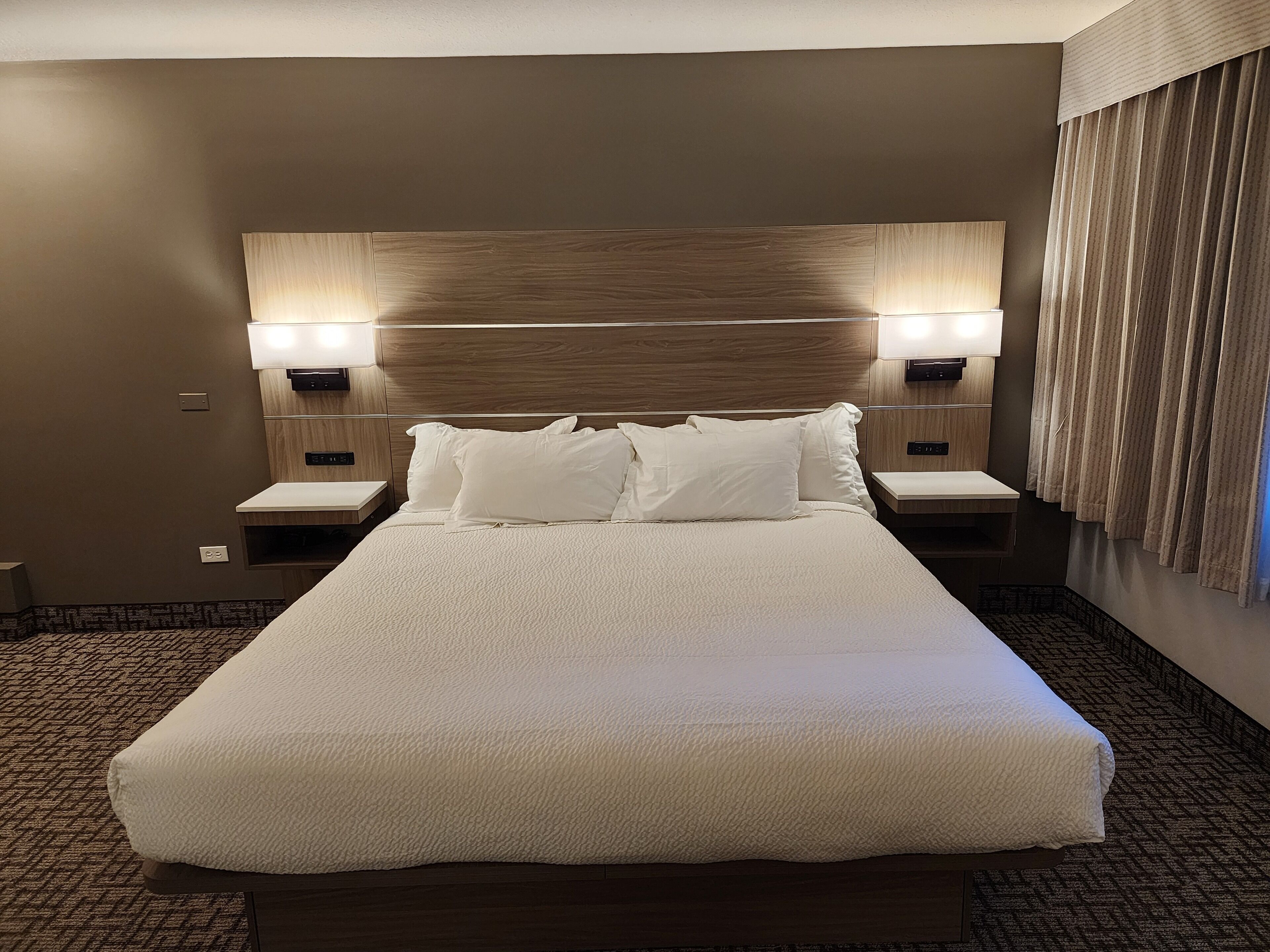A large bed with white linens, two bedside tables, and wall-mounted lamps.