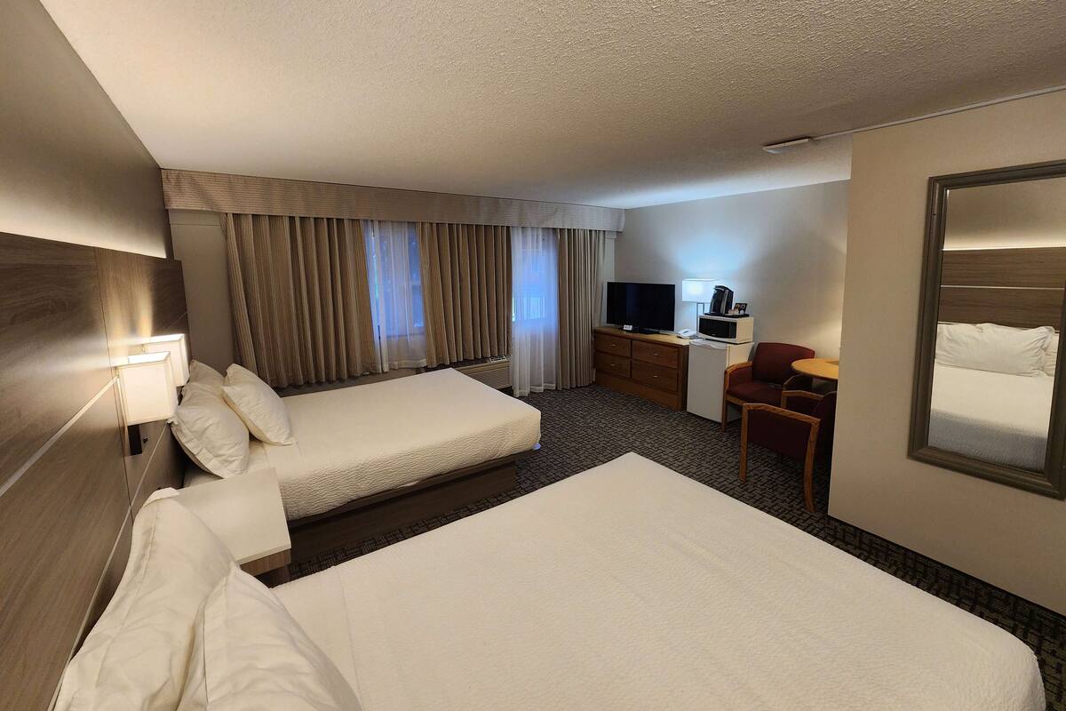 Una habitación de hotel con dos camas, un escritorio con televisor, una silla y un espejo grande.