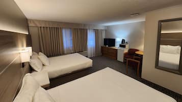 Una habitación de hotel con dos camas, un escritorio con televisor, una silla y un espejo grande.