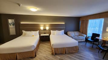 A hotel room with two beds, a sofa, a chair, a desk, and a window with curtains.