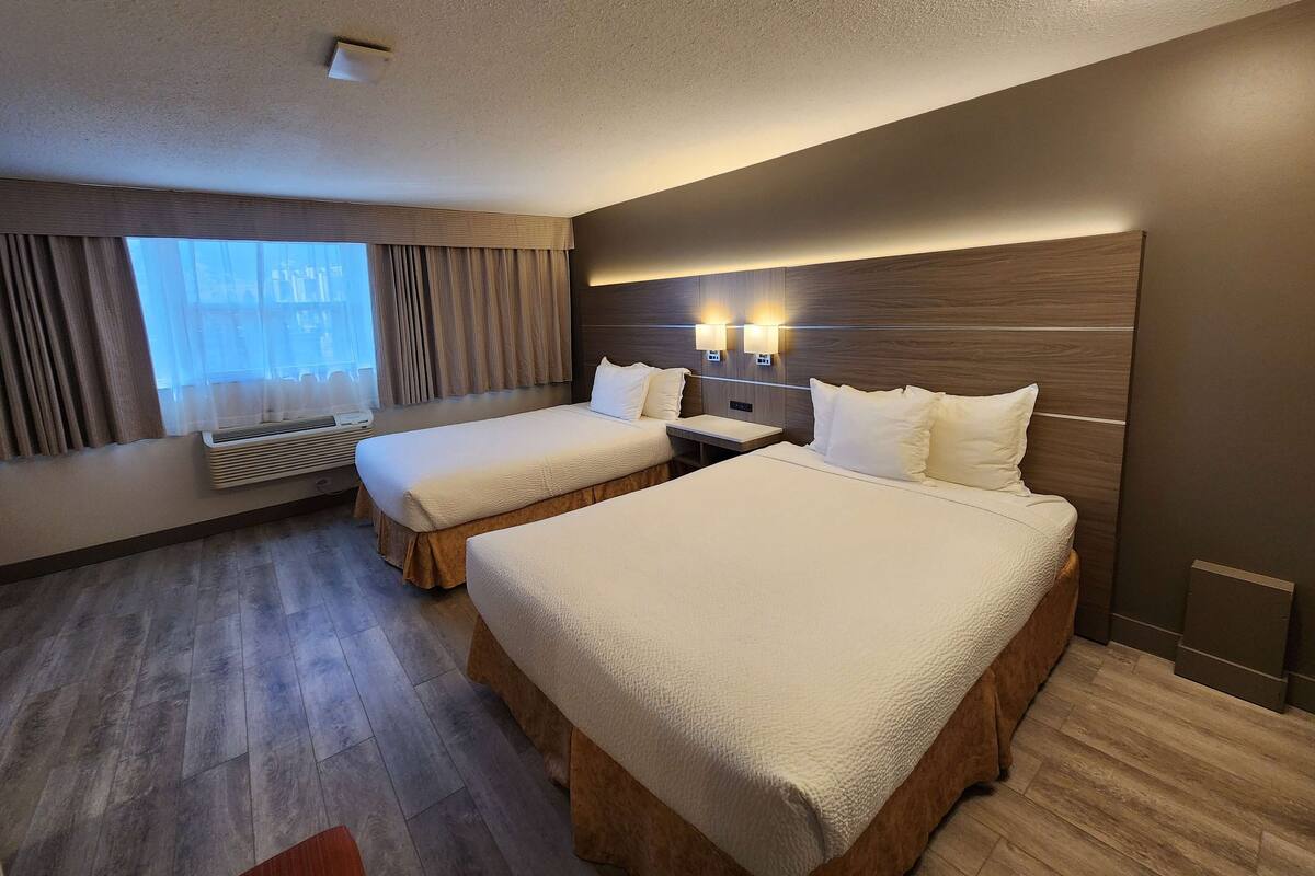 Habitación de hotel con dos camas, un ventanal con cortinas, suelo de madera y luces fijadas a la pared.