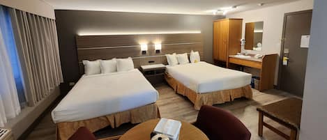 Een hotelkamer met twee bedden, een houten tafel, een stoel, een kitchenette en een badkamer met spiegel en kast.
