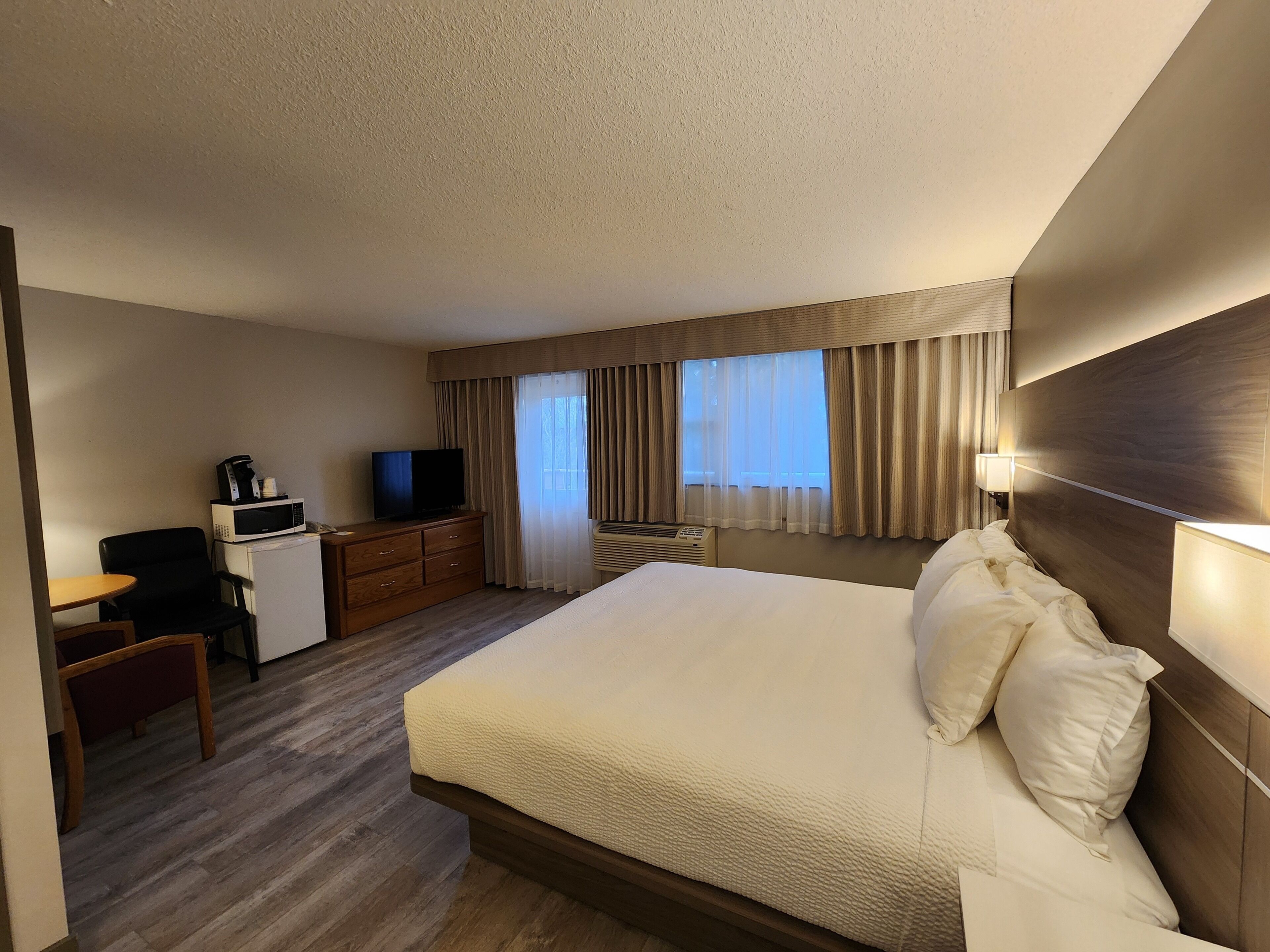 Una habitación de hotel con cama, escritorio con televisor y microondas, una silla y ventana con cortinas.