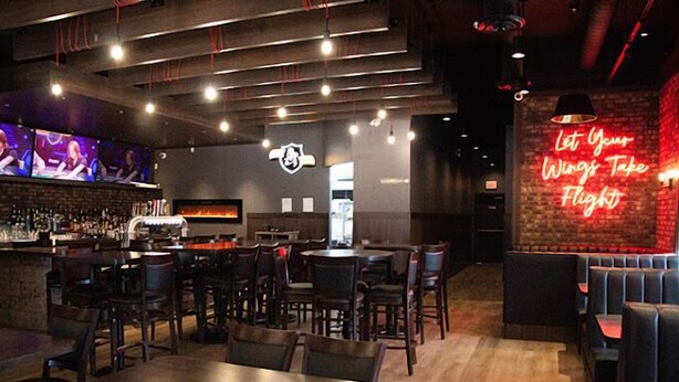 L’intérieur d’un restaurant, avec des banquettes, des tables, un bar et un panneau lumineux au néon sur le mur.