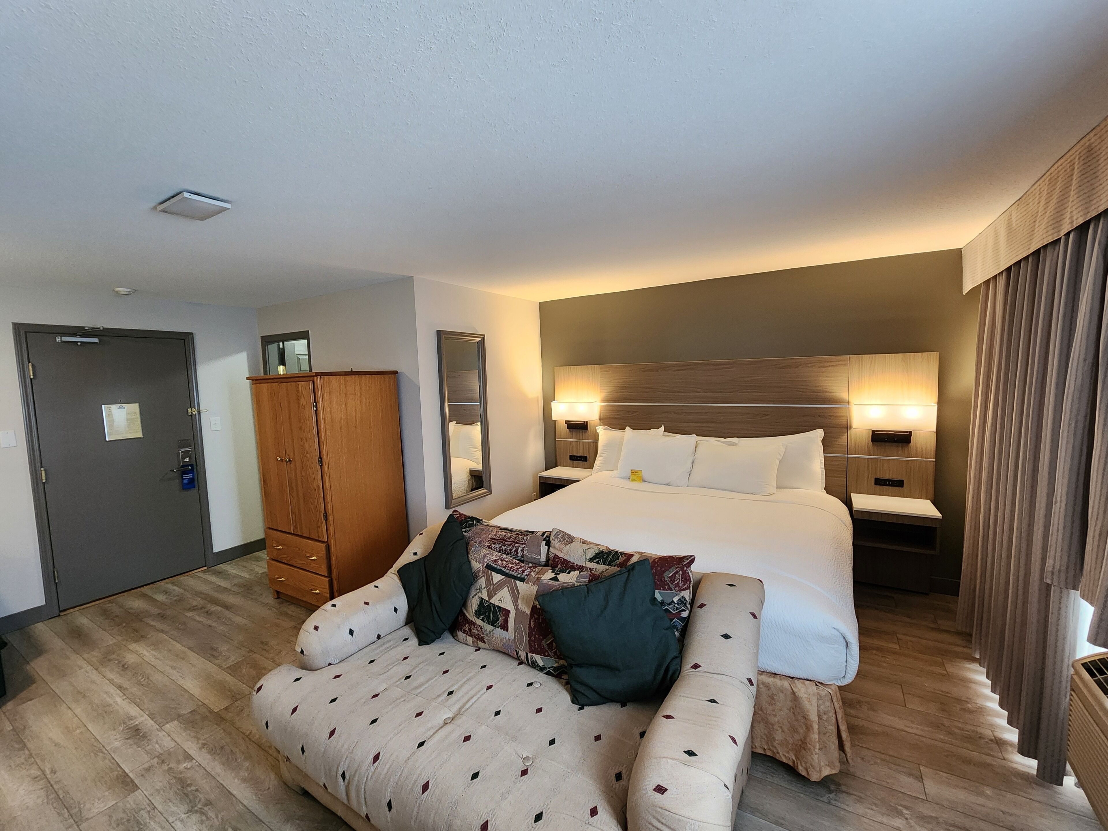 A hotel room with a bed, a wooden wardrobe, a sofa, and a bedside table.