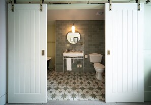 A bathroom with a star-patterned floor, a white sink, a toilet, and a mirror with a light above it. - Eleven Didsbury Park (Manchester)