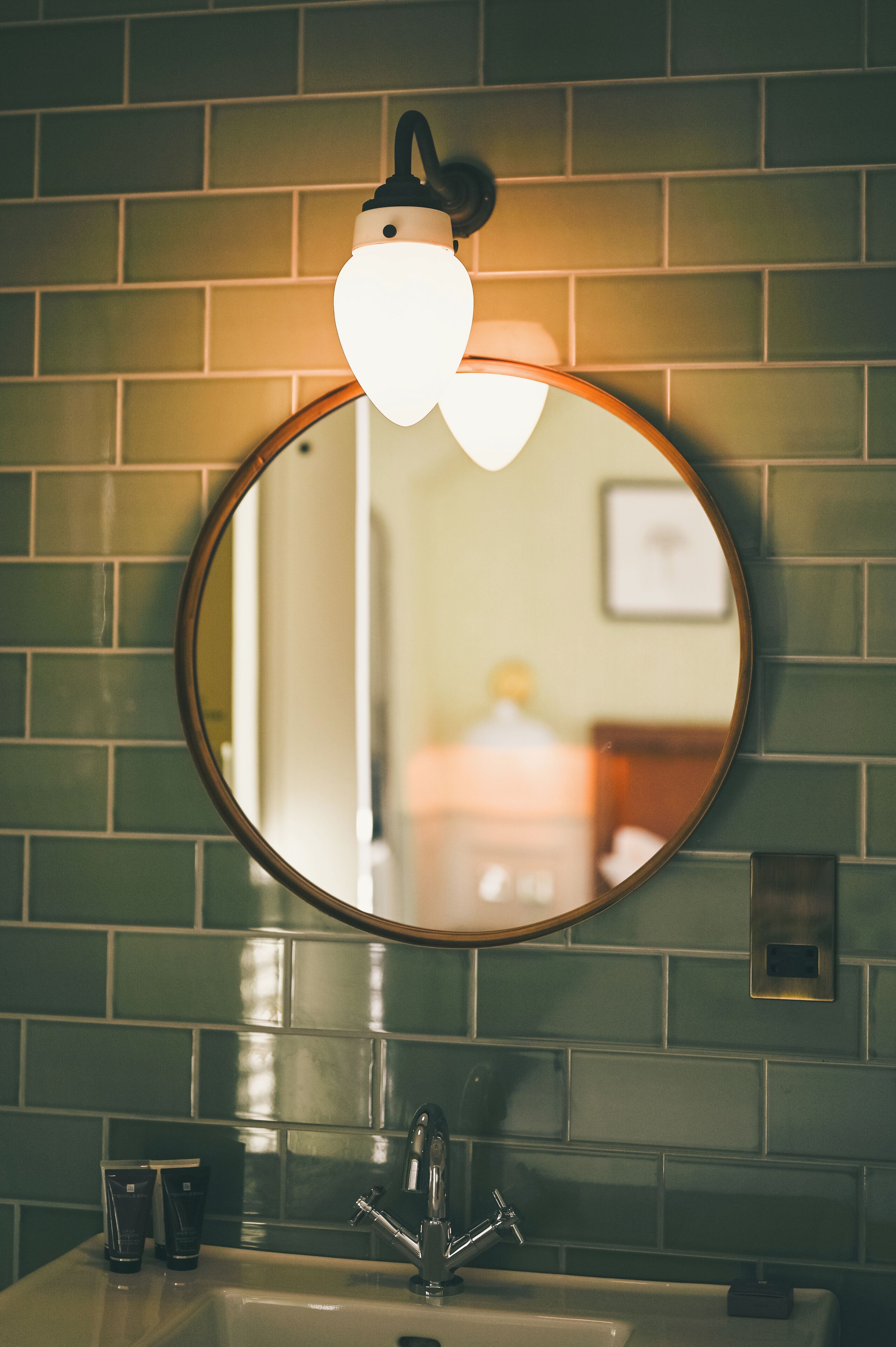 A bathroom with a round mirror, a light fixture above the mirror, and a sink with a faucet.
