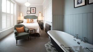 A bedroom with a large bed, a green armchair, a nightstand, a lamp, a radiator, and a bathtub. - Eleven Didsbury Park (Manchester)