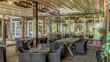 An outdoor patio area with wicker furniture, tables, and a glass enclosure.