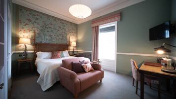 A hotel room with a bed, a sofa, a desk with a lamp, a chair, a television, and a window with curtains.