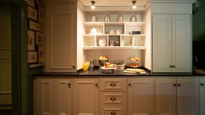 A kitchen with white cabinetry, a black countertop, and various food items displayed on shelves. - Eleven Didsbury Park (Manchester)