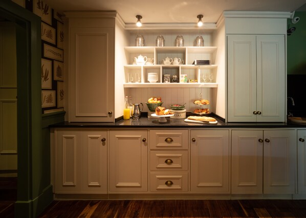 A kitchen with white cabinetry, a black countertop, and various food items displayed on shelves. - Eleven Didsbury Park (Manchester)