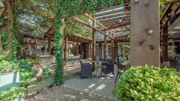 A covered outdoor patio with wooden beams, stone flooring, and wicker furniture.