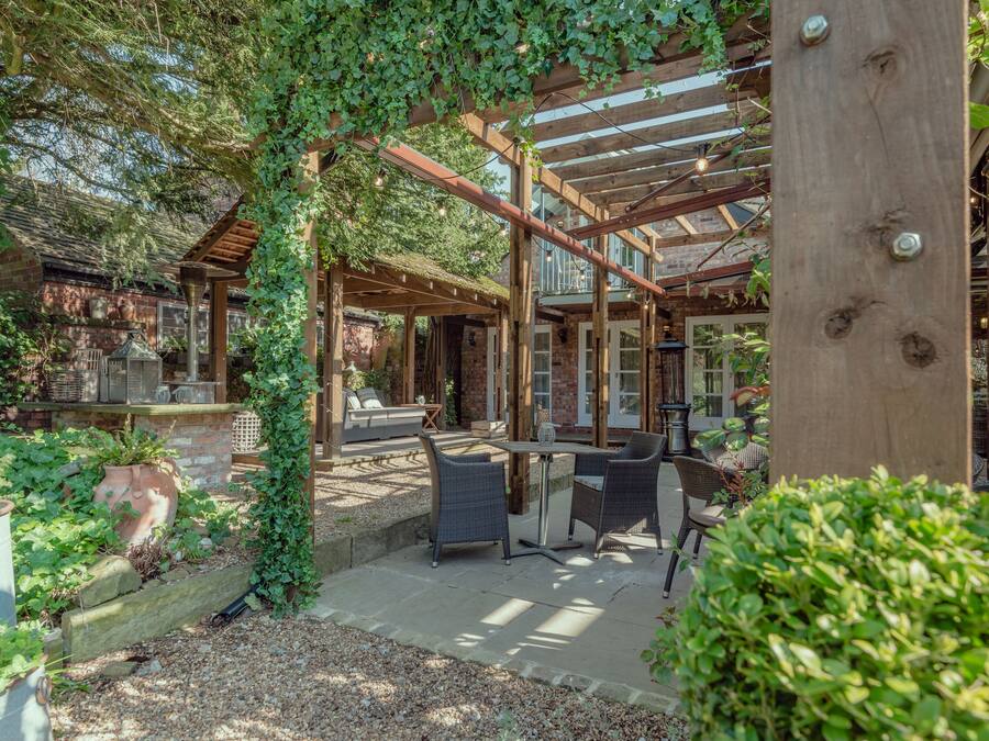 A covered outdoor patio with wooden beams, stone flooring, and wicker furniture.