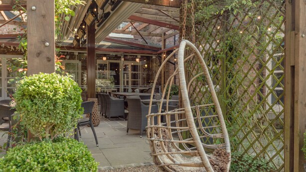 A wicker swing chair in a garden area with a brick wall and greenery. - Eleven Didsbury Park (Manchester)
