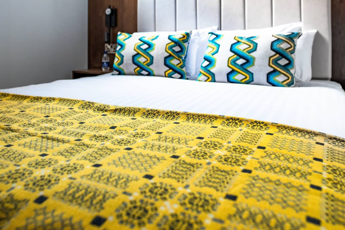 A hotel room with a bed, patterned pillows, a headboard, and a window with curtains.
