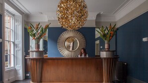 Un comptoir d’accueil agrémenté d’un grand miroir, de deux plantes en pot et d’un tapis à motifs.
