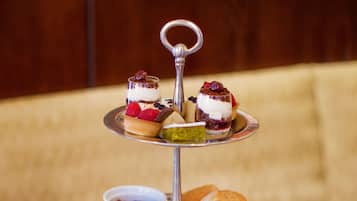 A three-tiered dessert stand with sandwiches and pastries on a round table.