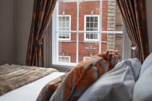 Enjoy a view of the High Pavement building from the comfort of this room, featuring a bed with a cozy throw and leaf-patterned curtains.