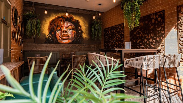 L’intérieur d’un restaurant avec des murs en briques, des plantes suspendues et des chaises en osier.