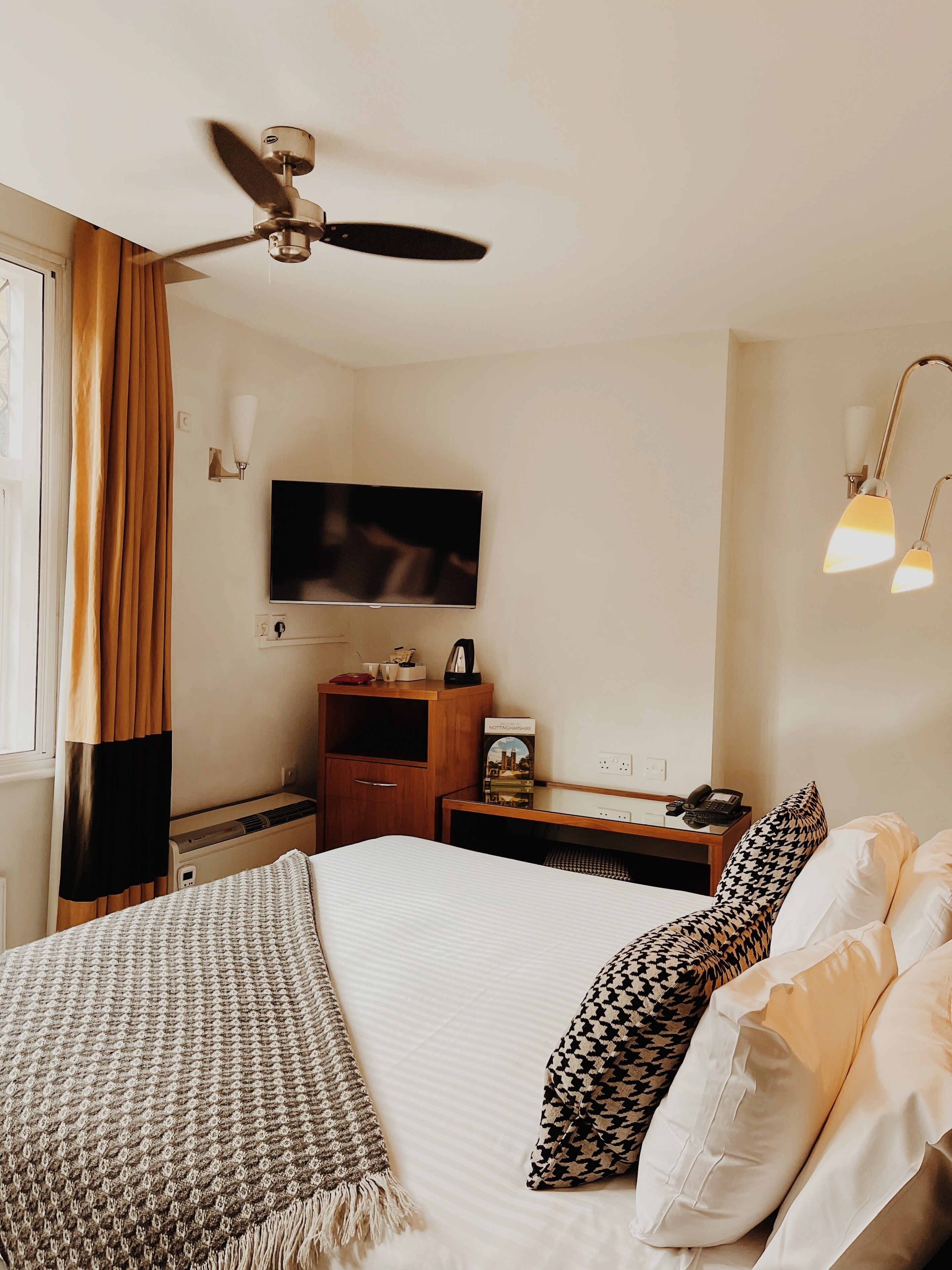 A hotel room with a bed, a TV, a desk, a lamp, and a ceiling fan.