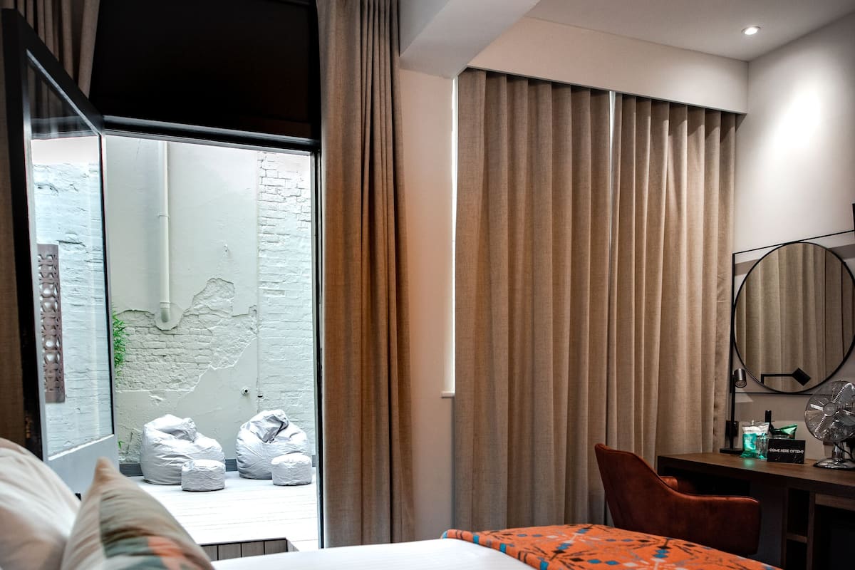 A hotel room with a bed, a desk, a chair, and a large window with curtains.
