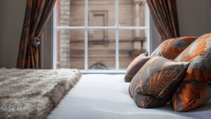 Un lit avec une couverture moelleuse et des coussins à motifs, une fenêtre avec des rideaux et une vue sur un bâtiment à l’extérieur.