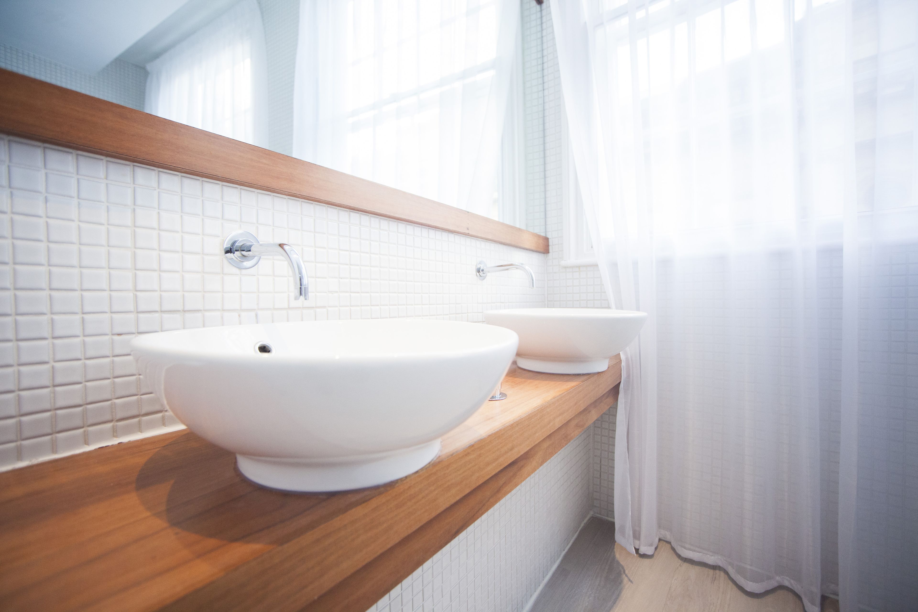 Un baño con dos lavamanos blancos, encimera de madera y un espejo sobre los lavamanos.