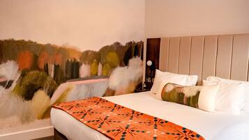 Una habitación de hotel con una cama, cabecera, un mural en la pared y una lámpara de techo.