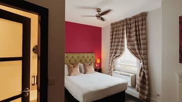 Quarto de hotel com cama, ventoinha no teto, janela com cortinas e vista para o exterior.