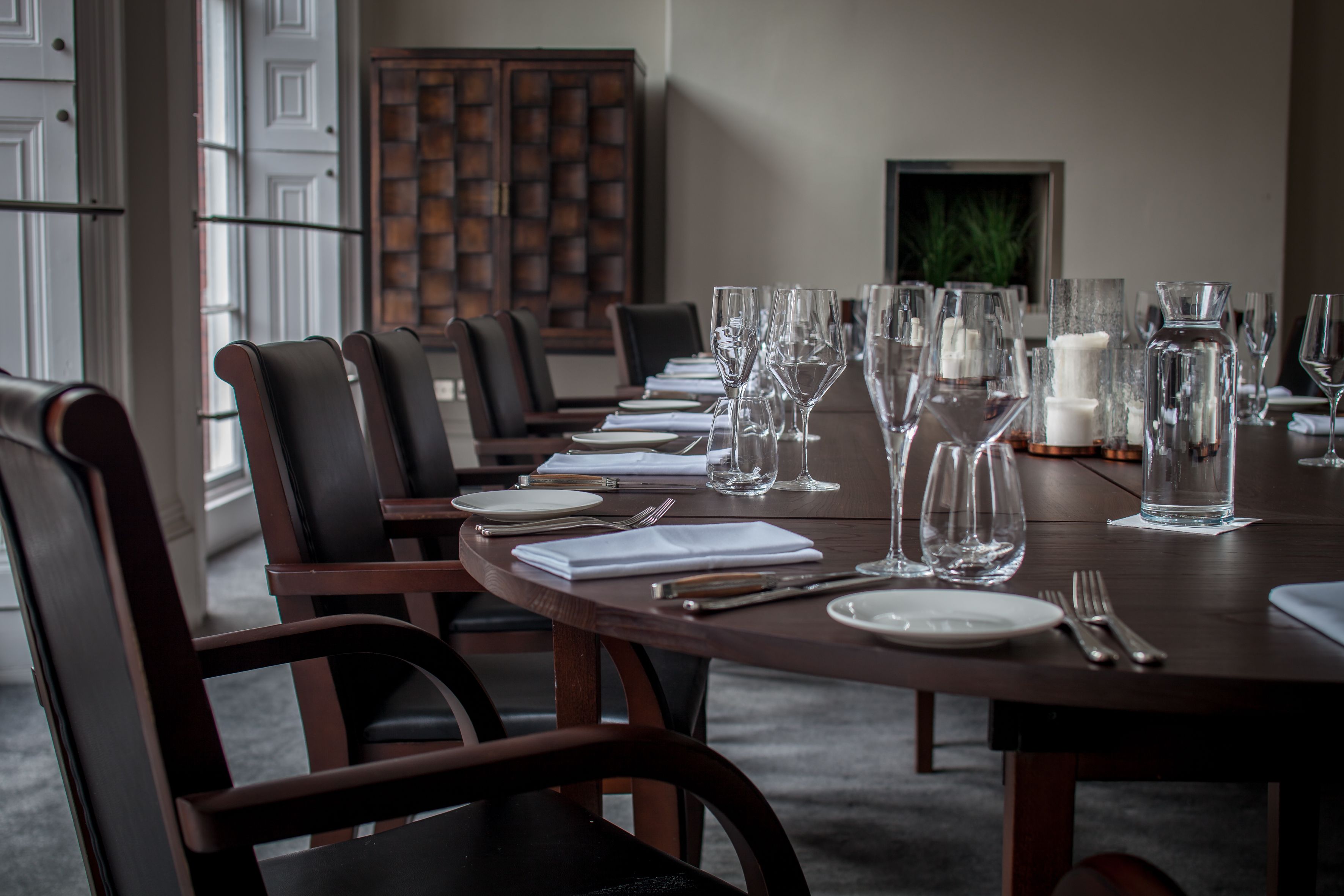 Une table à manger, accompagnée de chaises, d’assiettes, de couverts et de verres à vin, dans une salle à manger élégante.