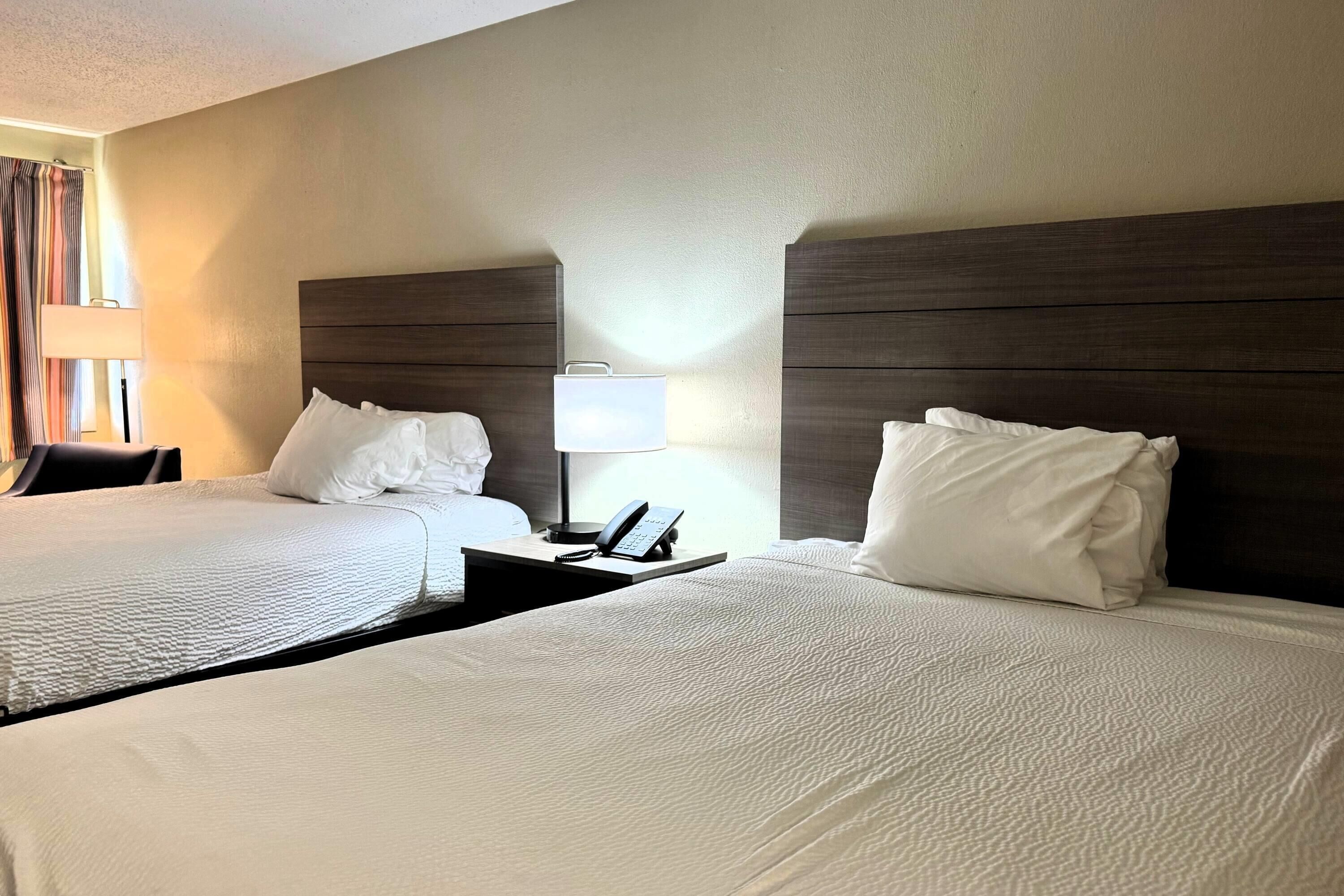 A hotel room with two beds, a nightstand with a lamp, and a telephone.
